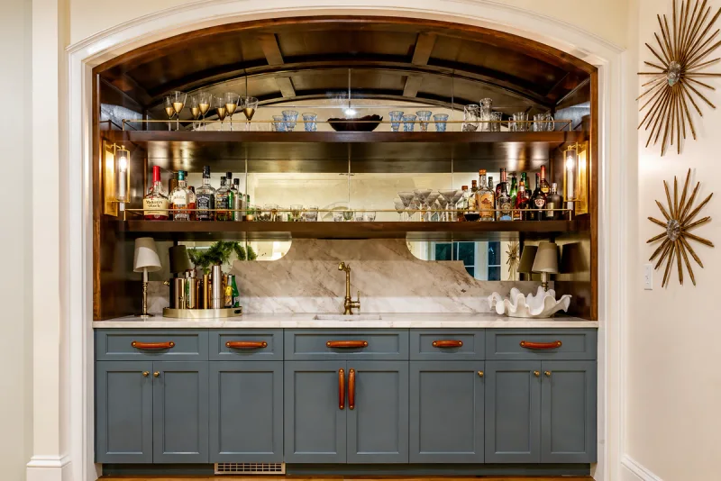 Home bar with slate-blue painted cabinetry, leather pulls and a marble counter