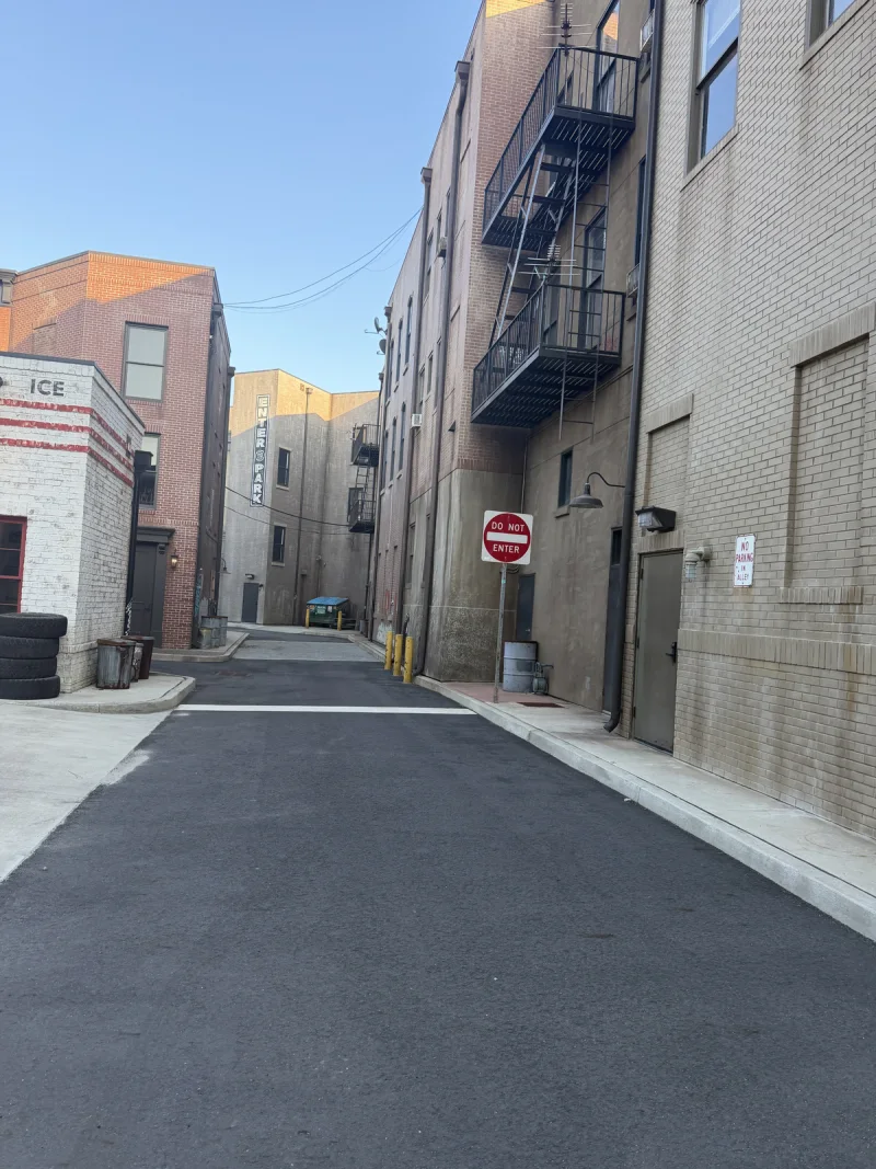 Narrow service lane between the painted mixed-use buildings and neighboring brick facade