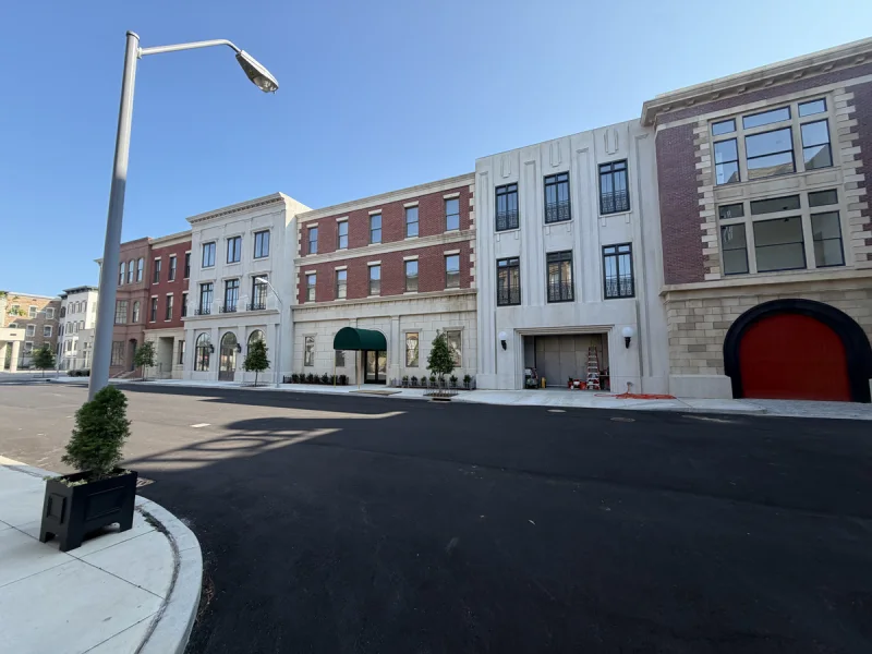 Mixed-use block seen from the street, with painted stone facades, an awning and arched red doors