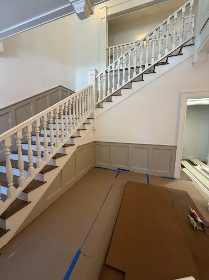 Staircase with white-painted balusters and greige wainscot panelling, floors covered during finishing