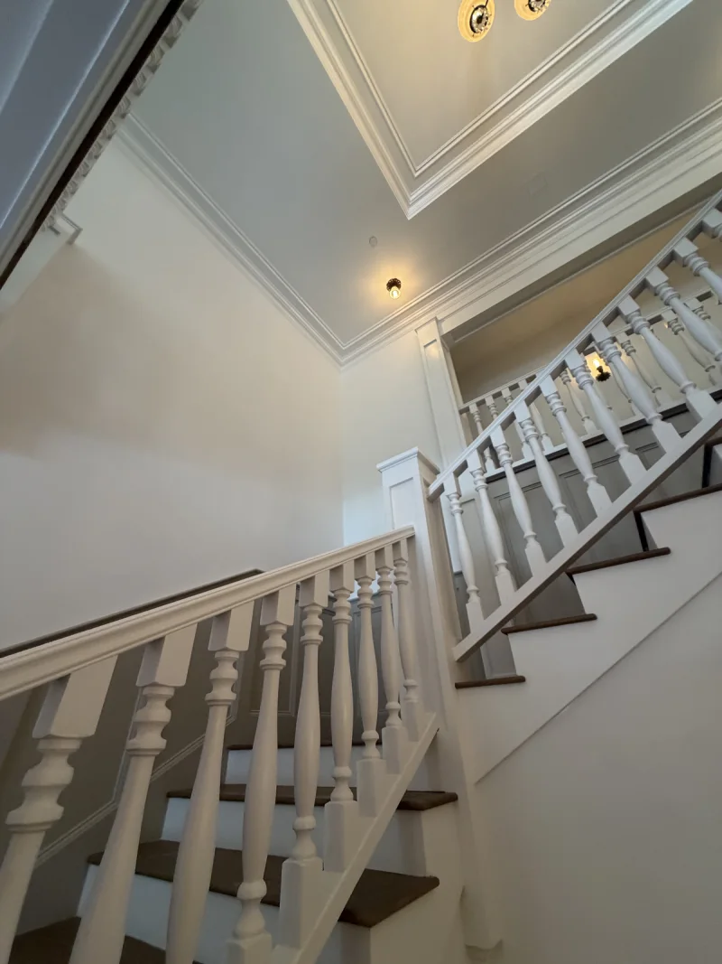 Stairwell painted in soft white with turned balusters and layered crown molding