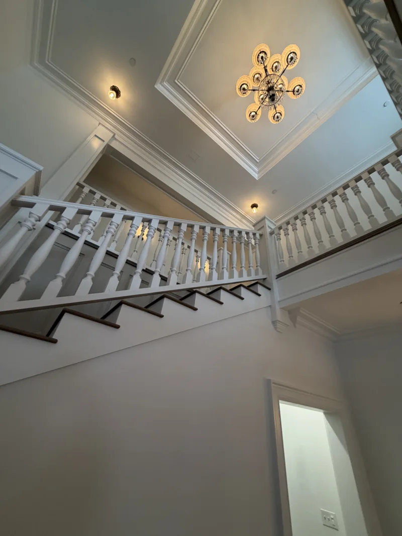 Upper landing balustrade and recessed ceiling painted white beneath a starburst chandelier