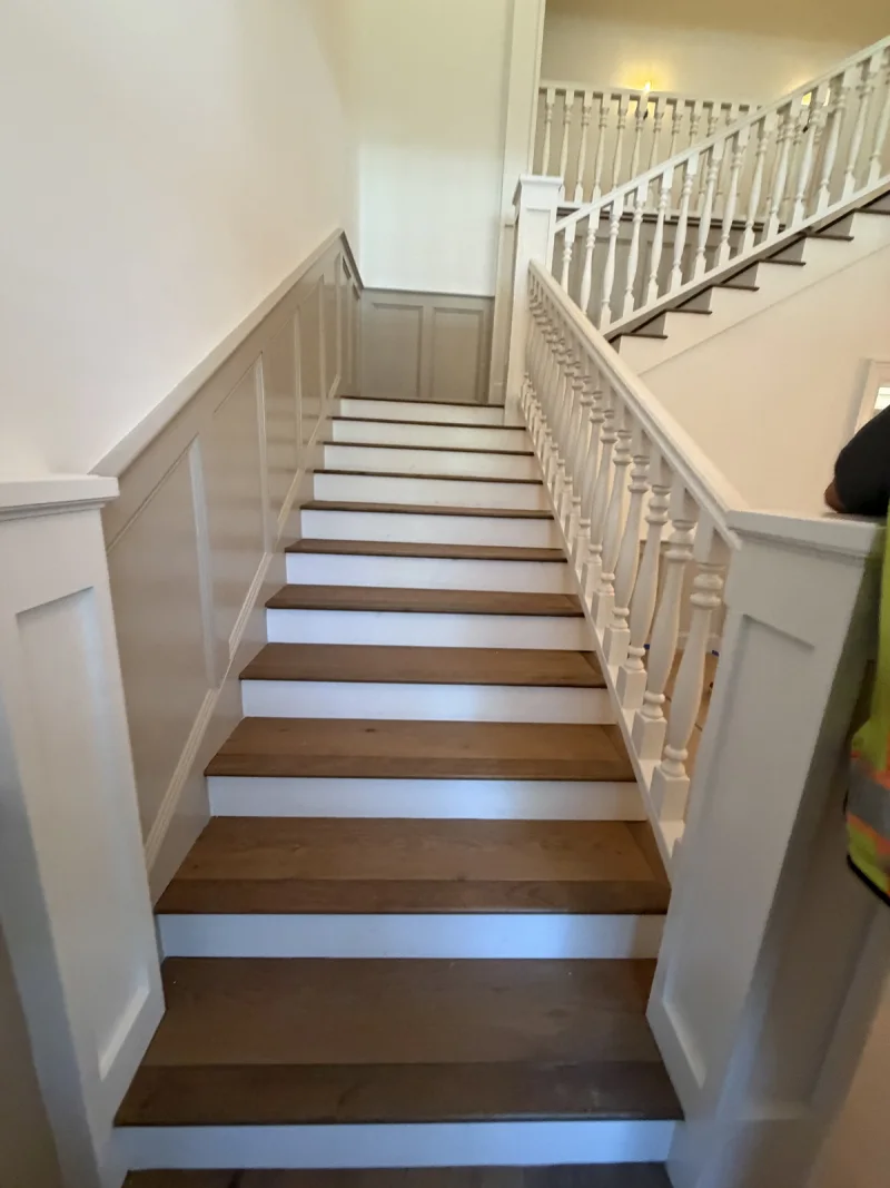 Straight stair run framed by white board-and-batten wainscoting above stained wood treads