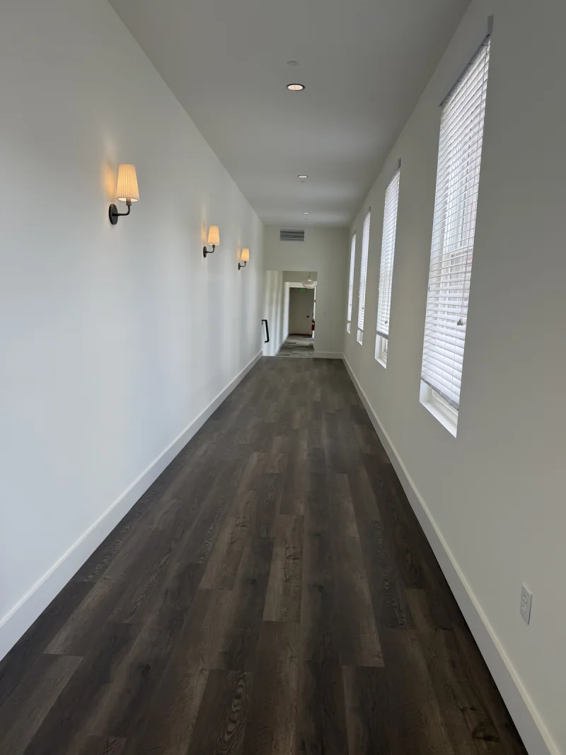 Hallway finished in flat white with wall sconces above dark plank flooring