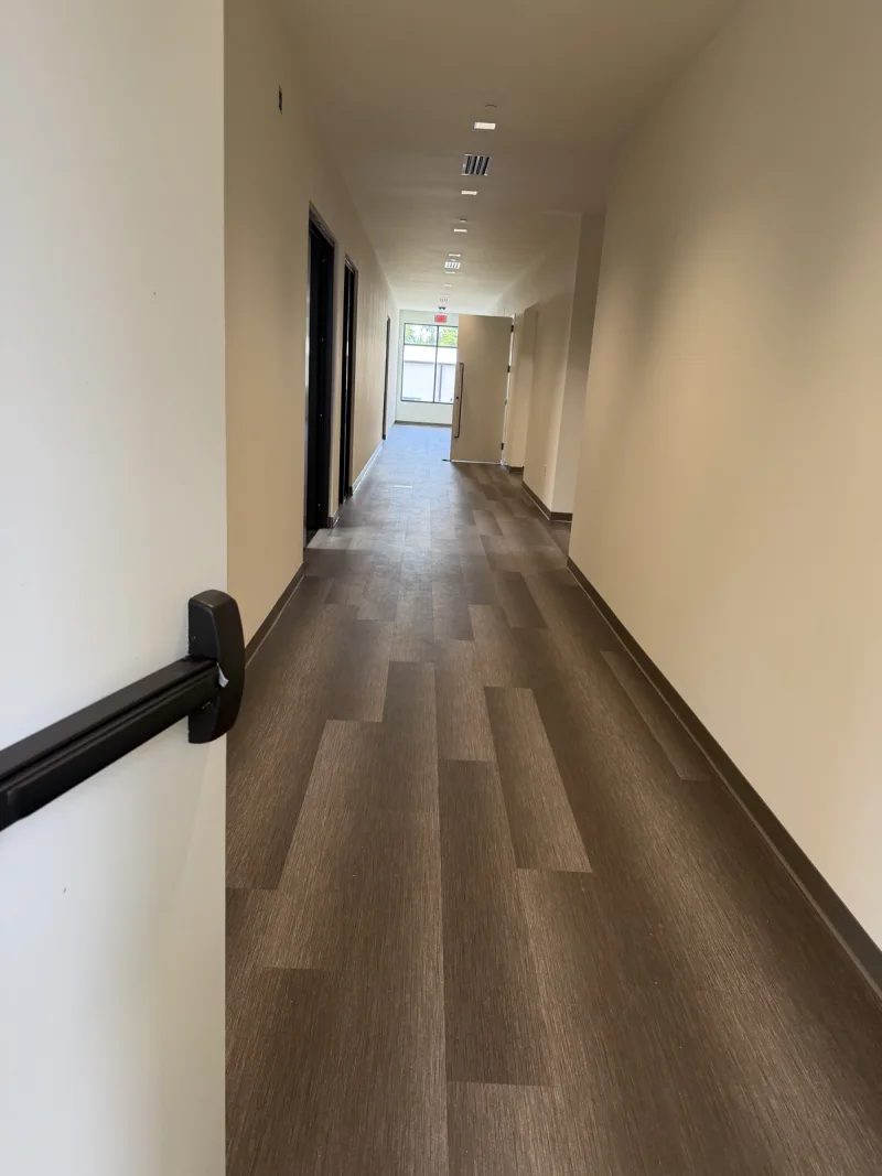 Corridor with painted white walls and dark door frames leading toward a glazed exit