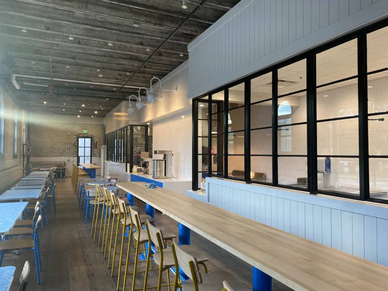 Long bar counter and stools against exposed brick, with blue painted bases below