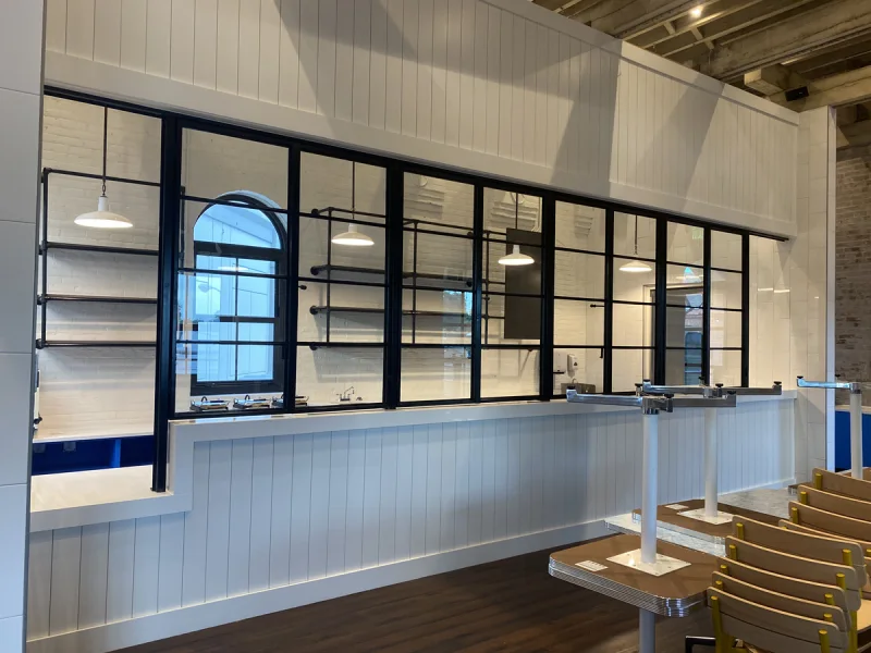 Café service counter in white shiplap framed by black steel windows and pendant lighting