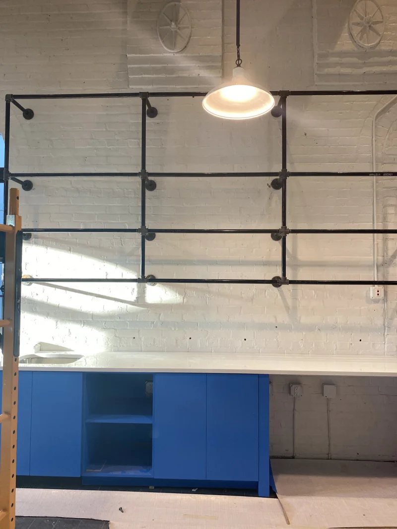 White painted brick wall with black steel shelving mounted above blue cabinetry