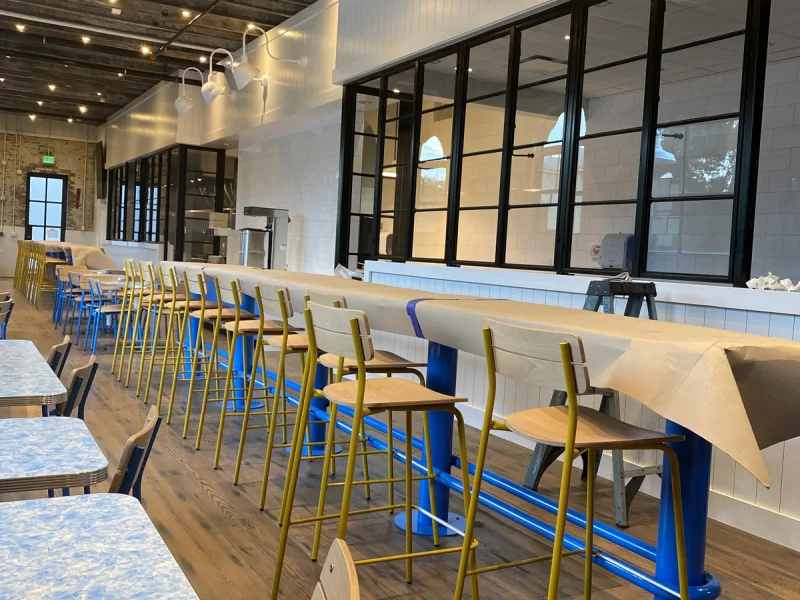 Full café dining room with long counters, blue seating and black framed service windows