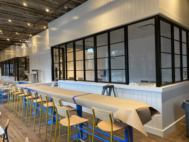 Dining counter and built-in bench beneath black steel windows and pendant lights
