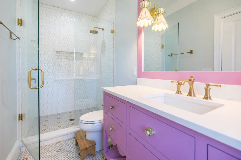 Bathroom with an orchid-painted vanity, soft pink accent wall and a glass shower enclosure